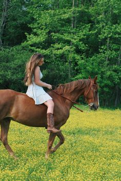 a woman riding on the back of a brown horse in a field of yellow flowers