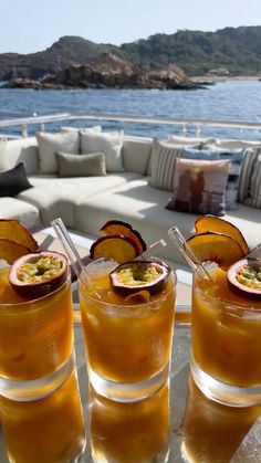 three glasses filled with drinks sitting on top of a table next to the ocean and mountains