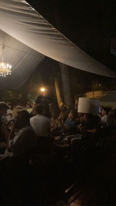 a group of people sitting under a white tent at night with chandelier hanging from the ceiling