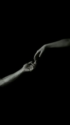 two hands reaching out towards each other in the dark with one hand holding the other's hand