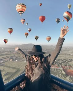 a woman with her hands up in the air surrounded by hot air balloons flying overhead