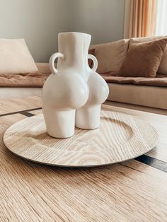 two white vases sitting on top of a wooden table in front of a couch