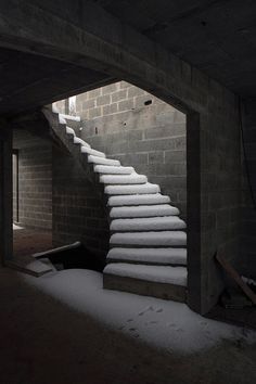 snow is piled up on the stairs in an empty room with brick walls and concrete flooring