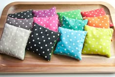 six different colored pillows sitting on top of a wooden tray with polka dot print fabric