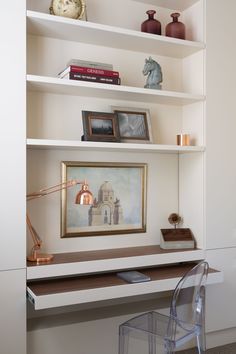 a desk with a chair and pictures on the shelves above it in front of a clock