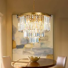 a chandelier hanging over a dining room table with white chairs and a painting on the wall behind it