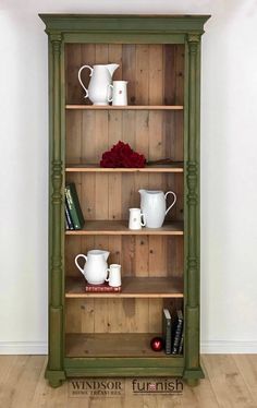 a green bookcase with cups and mugs on it in front of a white wall