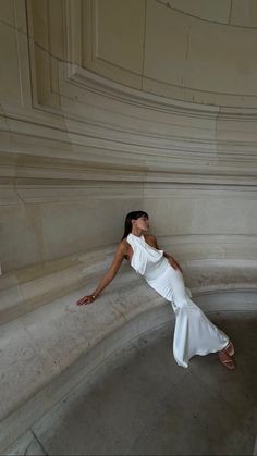 a woman in a white dress leaning against a wall with her hands on the ground