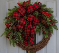 a wreath with red and black plaid bows hanging on a door