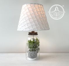 a lamp that is on top of a table with plants in the jar underneath it