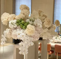 a vase filled with white flowers and greenery on top of a table in a room