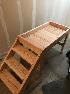 a wooden step stool sitting on top of a cement floor next to a wall and stairs