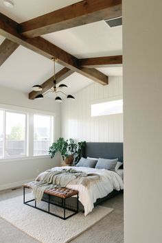 a bedroom with white walls and wood beams, carpeted flooring, and a large bed