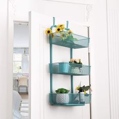 a wall mounted shelf with three baskets and flowers on the top, in front of a white door