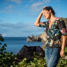 a woman standing in front of the ocean with her hands on her head and looking down