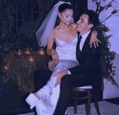 a bride and groom sitting on a chair in front of a house with candles lit up behind them