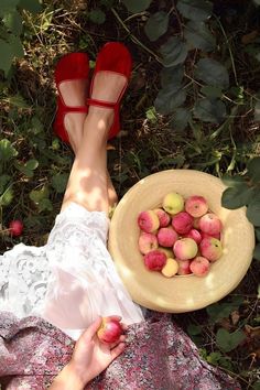 a woman laying on the ground with her feet up next to a bowl of apples