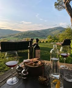 an outdoor table with wine glasses and food on it in front of a scenic view