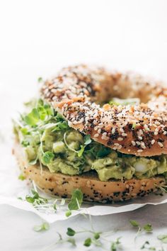 an avocado bagel sandwich with sesame seeds and sprouts on top