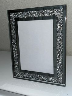 a black frame with silver glitter on the edges and a white sheet of paper underneath