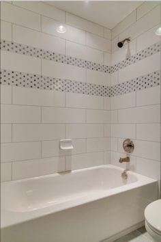 a white bathtub sitting next to a toilet in a bathroom with tile on the walls