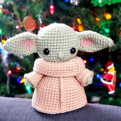 a crocheted baby yoda doll sitting in front of a christmas tree