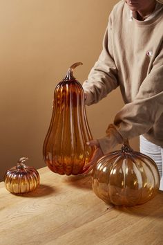 a person is holding two glass pumpkins on a wooden table with another one in the background