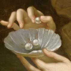 a close up of a person holding a shell with pearls in its palm and two hands