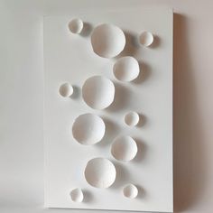 an art work with white balls and circles on a sheet of paper that is hanging on the wall