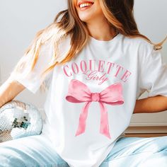 Get girly and flirty with the Coquette Girly Tee! This tee features a big pink bow and a playful "Coquette Girly" text, perfect for adding a touch of fun and femininity to your wardrobe. Stand out from the crowd with this quirky and stylish tee! Design is Printed Direct to Garment. Pink Sorority T-shirt For Spring, Pink Graphic Tee For Gender Reveal, Cute Summer T-shirt With Pink Bow, Pink T-shirt With Bow For Summer, Cute Pink Party T-shirt, Cute Spring T-shirt For Gender Reveal, Cute T-shirt For Spring Gender Reveal, Pink Crew Neck T-shirt With Bow, Cute Pink T-shirt With Bow Detail