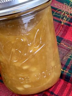 a glass jar filled with liquid sitting on top of a plaid table cloth next to a metal lid