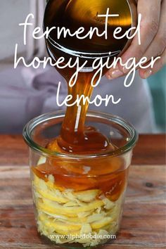 someone pouring honey into a glass jar filled with lemons and other ingredients to make homemade honey