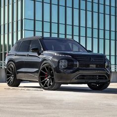 the front end of a black suv parked in front of a tall building with glass windows