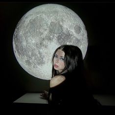 a woman sitting in front of a large moon