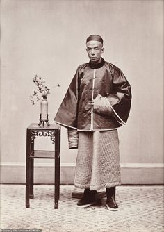 an old photo of a man standing next to a table with a vase on it