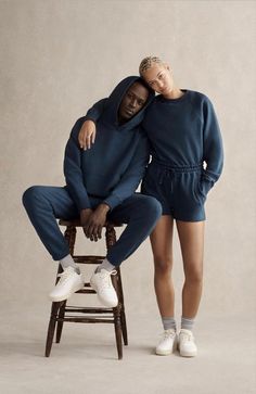 two people sitting on a chair with their arms around each other and one person standing up