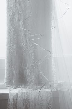 a white curtain hanging in front of a window next to a window sill with sheer curtains