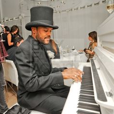 a man wearing a top hat and playing the piano in a room full of people