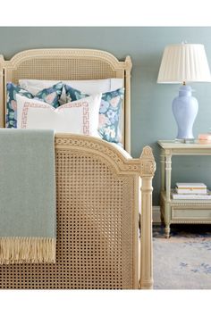 a wicker bed with blue and white pillows on the headboard, next to a lamp