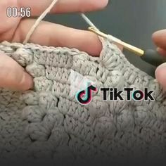 someone crocheting the ends of a blanket with a pair of hands holding a knitting needle