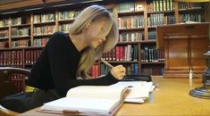 a woman sitting at a table in front of a bookshelf