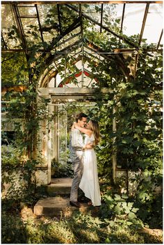 a man and woman standing in front of an arch covered with greenery at their wedding