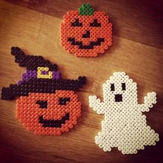 two halloween coasters made out of perler beads on a wooden table with a pumpkin and ghost