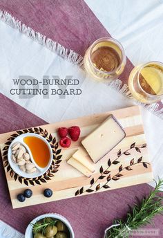 a wooden cutting board topped with cheese and fruit next to bowls of olives, raspberries and honey