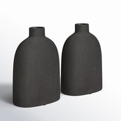 two black vases sitting next to each other on a white surface, one is made out of concrete