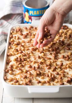 a person dipping peanuts into a casserole dish