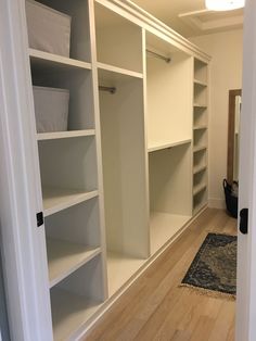 an empty walk in closet with white shelving and baskets on the shelves, next to a rug