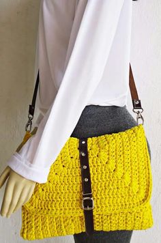 a woman holding a yellow crocheted purse on top of a mannequin's head