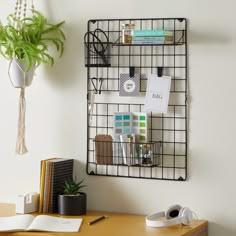 a desk with a plant, books and office supplies on it next to a white wall