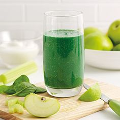 a glass filled with green liquid next to sliced apples